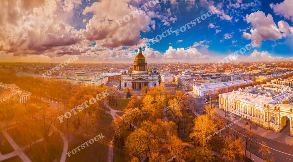 На фотографии изображён Исаакиевский собор — величественный символ Санкт-Петербурга, окружённый весенними деревьями. Съёмка выполнена с высоты, что позволяет оценить красоту архитектурного ансамбля и гармоничное расположение зданий вокруг собора. Вдали видны исторические строения, в том числе Адмиралтейство, дополняющие городскую панораму. Тёплые краски закатного неба и свет создают атмосферу уюта и романтики весеннего Петербурга.